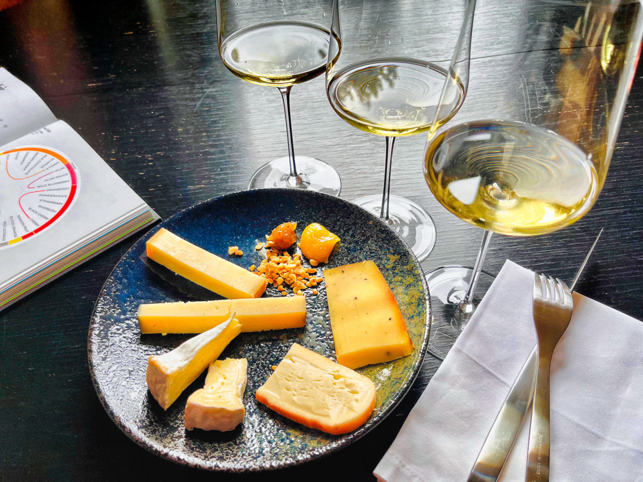 Verschieden Käsesorten und drei Weingläser mit Weißwein